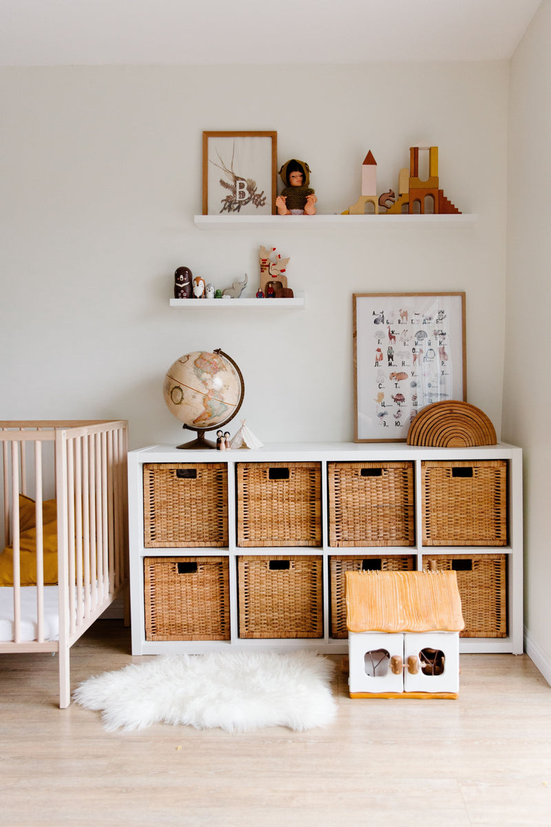A tidy child's bedroom with wooden shelves, wicker storage baskets, soft toys and a made bed in warm neutral tones